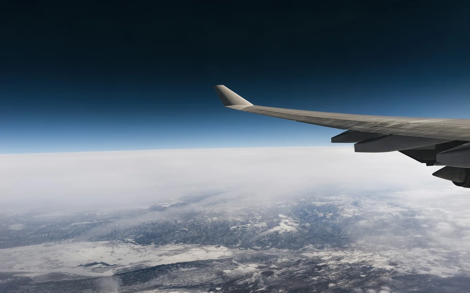 Flygplansvinge och moln sedda genom ett flygplansfönster.